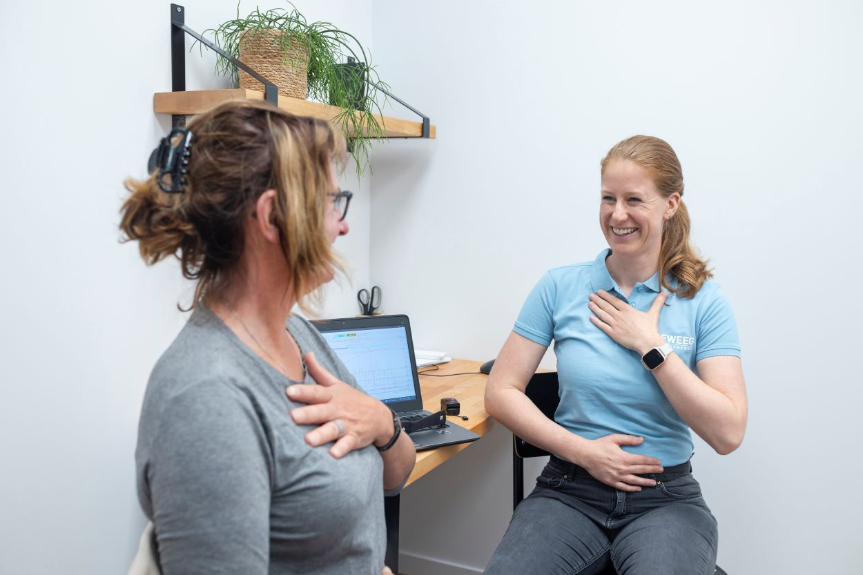 Fysio in de praktijk met patient die hand op de borst heeft