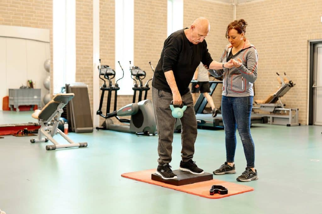 Oudere man doet balansoefening met fysio vrouw