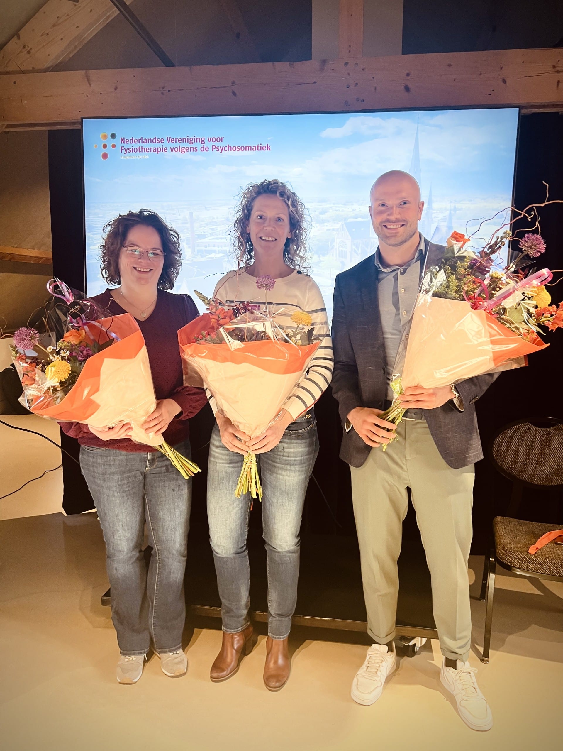 Twee vrouwen en een man met bloemen in hun hand